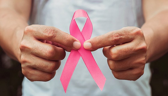 Person holds pink ribbon in front of camera lens in support of breast cancer research